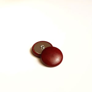 May include: Two red wooden buttons with a silver shank. The buttons are round and have a smooth surface.