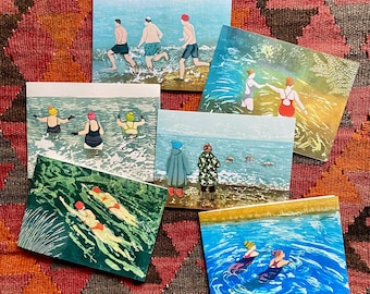 May include: A collection of six rectangular greeting cards featuring colorful illustrations of people swimming and wading in the ocean. The scenes depict various individuals in swimwear, hats, and coats interacting with blue water, waves, and sandy shorelines.