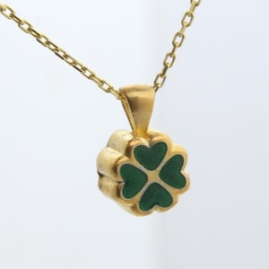 May include: A gold necklace with a four-leaf clover pendant. The pendant is gold with four green heart-shaped leaves. The chain is a delicate gold link chain. The necklace is displayed against a white background.