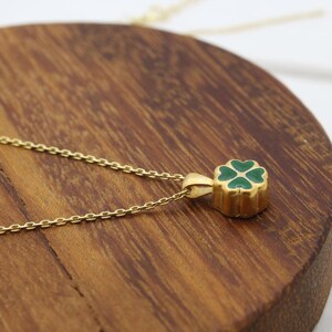 May include: A gold-colored necklace with a four-leaf clover pendant. The clover is green and set in a gold-colored frame. The necklace chain is delicate and gold-colored. The pendant is approximately 0.5 inches in diameter.