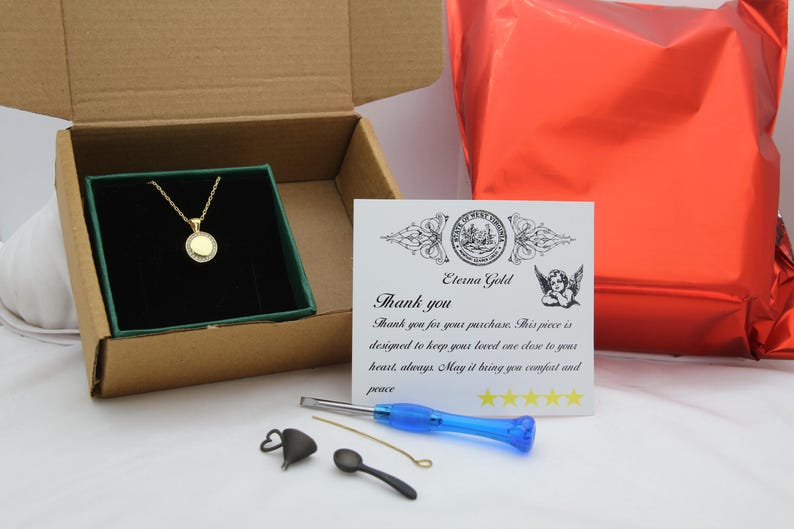 May include: A gold-colored necklace with a circular pendant, presented in a box with a green interior. The box is open, revealing the necklace. A card with text and a red package are also visible.
