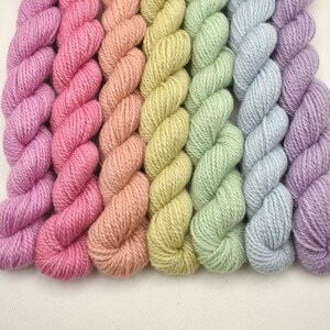May include: A collection of colorful yarn skeins arranged in a rainbow gradient. The colors include shades of pink, peach, yellow, green, blue, and purple. The yarn is tightly wound and appears soft, ideal for knitting or crochet projects.