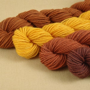 May include: Three skeins of yarn in different shades of brown and yellow. The yarn is arranged in a loose braid.