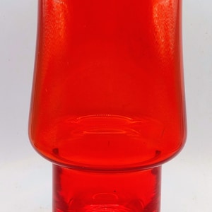 May include: A striking red glass vase with a distinctive two-part structure. The top section is a flared cylinder, and the base is a smaller, cylindrical form. The base's bottom is clear glass. This decorative vase is suitable for displaying flowers or as a standalone art piece.