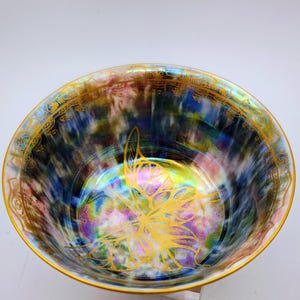 May include: A round ceramic bowl featuring an iridescent, multi-coloured finish with swirling patterns of blue, purple, and pink. The interior displays a prominent gold butterfly illustration at the centre and a decorative gold border along the rim.