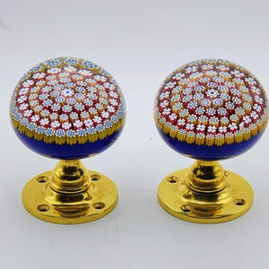 May include: Two spherical glass door knobs featuring a millefiori pattern with red, white, and blue floral motifs set against a deep blue base. Each knob is mounted on a polished gold-tone metal circular base with four pre-drilled screw holes.