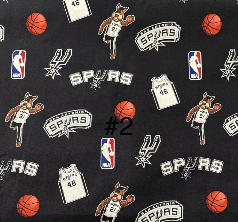 K&ouml;nnte beinhalten: Schwarzer Stoff mit einem sich wiederholenden Muster aus Logos des Basketballteams San Antonio Spurs, Trikots, Basketb&auml;llen und dem Teammaskottchen. Das Trikot hat die Nummer 46. Das NBA-Logo ist ebenfalls vorhanden.