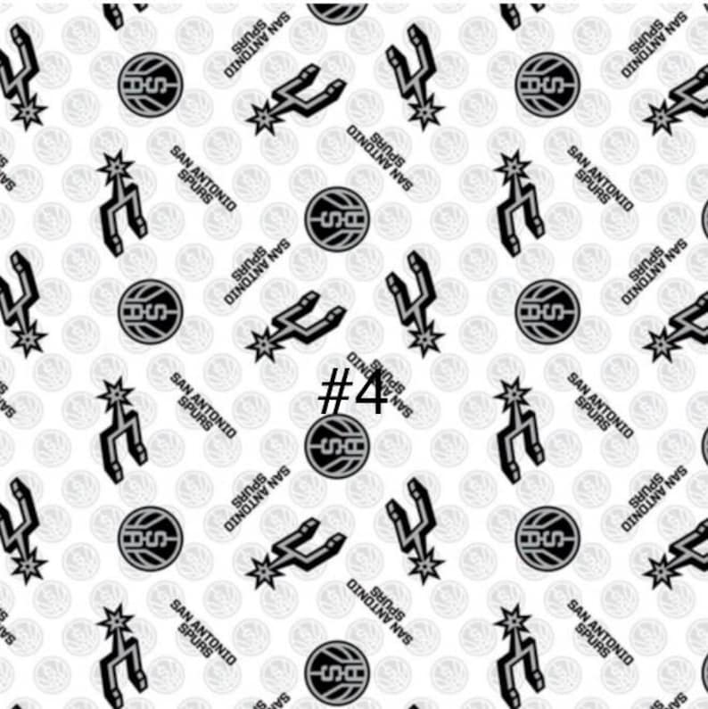 K&ouml;nnte beinhalten: Wei&szlig;er Stoff mit einem sich wiederholenden Muster aus schwarzen San Antonio Spurs Logos, Basketb&auml;llen und dem Text "SAN ANTONIO SPURS". Die Nummer "#4" ist ebenfalls sichtbar. Ideal f&uuml;r Sportprojekte.