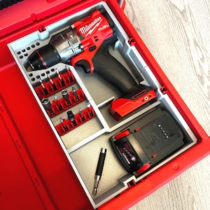 May include: A red Milwaukee FUEL drill and accessories are neatly organized inside a red toolbox. The set includes a drill, various bits, and a battery pack. The toolbox is designed to keep the tools secure and accessible.