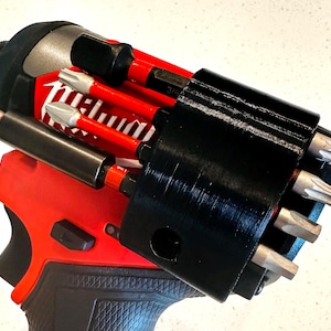 May include: A red and black power drill with a black bit holder attached. The bit holder contains several silver and red bits. The drill has the brand name "Milwaukee" printed on it.