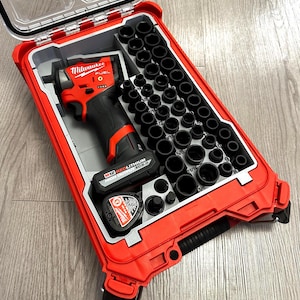 Puede incluir: Un juego de llaves de impacto Milwaukee M12 FUEL rojo y negro. El kit incluye una variedad de vasos negros, una batería y un cargador, todo ello alojado en un maletín de transporte rojo y duradero. El maletín está abierto, revelando las herramientas.