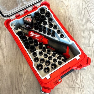 Può includere: Un kit di attrezzi Milwaukee FUEL rosso con coperchio trasparente, contenente un elettroutensile rosso e nero, bussole nere e una batteria. Il kit è organizzato in una custodia rossa con interno grigio.