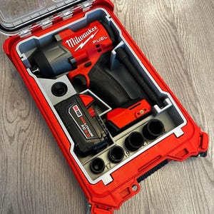 May include: A red Milwaukee FUEL impact wrench kit in a red and gray case. The kit includes the impact wrench, a battery, and several sockets. The case is open, revealing the tools neatly organized inside.