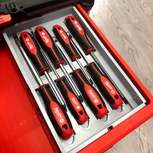 May include: A set of eight screwdrivers neatly arranged in a red toolbox drawer. The screwdrivers have black handles with red accents and the brand name "Milwaukee" printed on them. The drawer is gray and the toolbox is red.