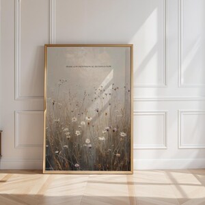 Op de afbeelding: Een ingelijste kunstdruk met een veld van wilde bloemen in zachte kleuren. Het kunstwerk heeft een gouden lijst en bevat de tekst "PRAISE GOD FROM WHOM ALL BLESSINGS FLOW" bovenaan. De print wordt tegen een witte muur getoond.