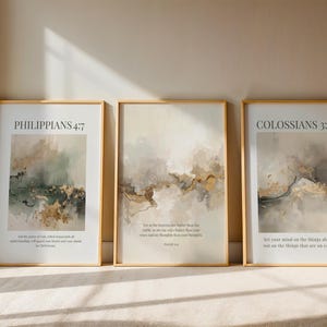 May include: Three framed art prints with gold frames. The prints feature abstract watercolor designs in neutral tones with gold accents. Each print has a Bible verse at the top and bottom. The text on the prints reads "PHILIPPIANS 4:7", "COLOSSIANS 3:2", and other text.