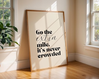 Könnte beinhalten: Ein gerahmter Druck mit dem Text "Go the extra mile, it's never crowded" in schwarzer Schrift. Der Druck hat einen cremefarbenen Hintergrund und einen goldenen Rahmen. Er lehnt an einer Wand in einem Raum mit Holzböden und einem Fenster.