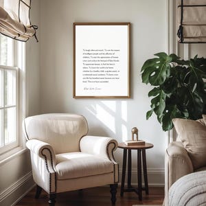 Puede incluir: Un marco dorado colgado en una pared blanca contiene texto negro sobre un fondo blanco. Debajo, un sill&oacute;n blanco con ribetes oscuros. Tambi&eacute;n se ven una peque&ntilde;a mesa de madera y una planta de interior.