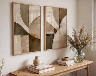 May include: Two framed abstract art prints with a geometric design in neutral tones of beige, brown, and olive green. The artwork hangs above a wooden table with a vase, books, and a bowl. A glass vase with dried flowers sits on the table.