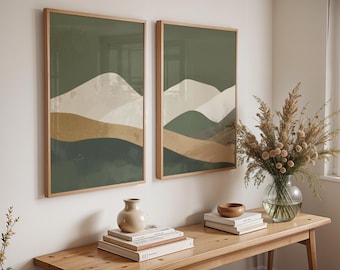 May include: Two framed landscape art prints with a mountain design in shades of green, beige, and white. The artwork is displayed on a white wall above a wooden table with decorative items.