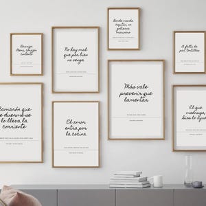 May include: A collection of framed wall art with various quotes in black script on a white background. The frames are a warm brown color, and the art is displayed on a white wall above a gray cabinet. The quotes are in Spanish.