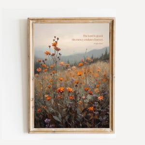 Puede incluir: Una lámina de arte enmarcada que muestra un campo de flores silvestres naranjas frente a un paisaje montañoso brumoso. El texto dice: The Lord is good; His mercy endures forever. Psalm 100:5. La obra está en un marco de madera clara.