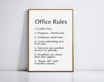 May include: A framed print with the text "Office Rules" in a black font. The rules include "Coffee first," "Progress > Perfection," and "Celebrate small wins." The print has a gold-colored frame and is displayed against a white wall.