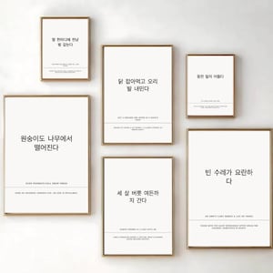 Op de afbeelding: Zes ingelijste kunstdrukken met goudkleurige frames worden op een witte muur getoond. Elke print bevat Koreaanse tekst op een witte achtergrond. De prints variëren in grootte en zijn aantrekkelijk gerangschikt.
