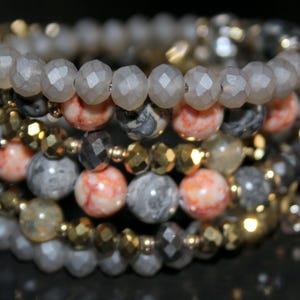 May include: A multi-layered bracelet featuring gray, white, and orange beads. The bracelet is made of various materials, including stone and metal.