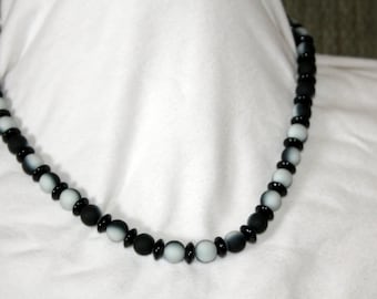 Op de afbeelding: Een zwarte en witte kralenketting met afwisselende zwarte en witte kralen. De kralen zijn rond en hebben een gladde, gepolijste afwerking.