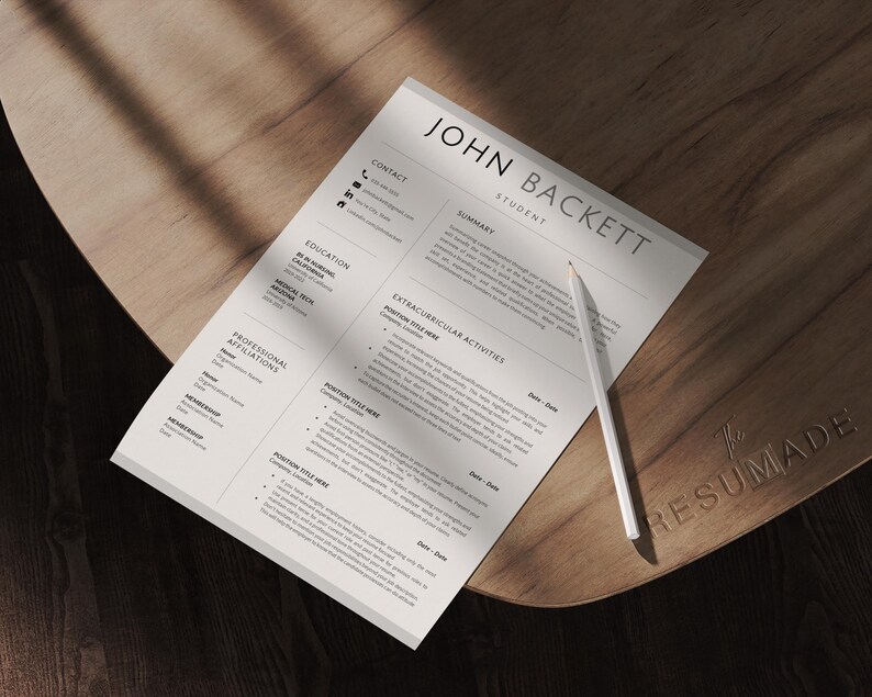 May include: A resume titled "JOHN BACKETT STUDENT" with a white pencil on a wooden surface. The resume includes sections for education, summary, and extracurricular activities. The wooden surface has the word "RESUMADE" engraved on it.