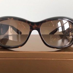 May include: Tortoise shell sunglasses with brown lenses. The sunglasses are sitting on a brown box.