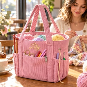 Peut inclure: Un sac de rangement pour pelotes en velours côtelé rose avec deux anses, portant le prénom brodé Lily sur le devant. Le sac comprend une poche frontale zippée, plusieurs poches latérales pour aiguilles et crochets, et un œillet passe-fil.