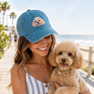 Può includere: Un cappellino da baseball blu con un ricamo raffigurante il muso di un barboncino marrone chiaro sul pannello frontale. Il cappellino presenta una visiera curva e una corona strutturata, con un dettaglio cucito di un cane dall'espressione felice.