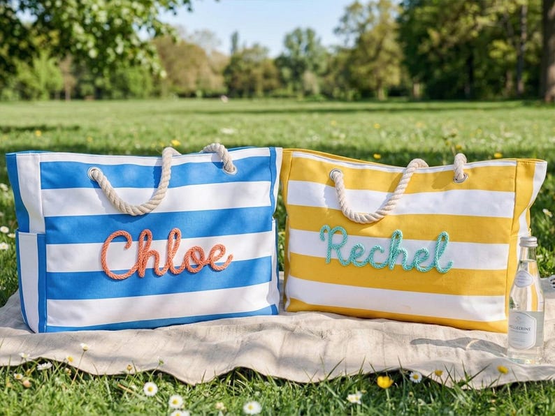 May include: Two striped tote bags with rope handles on a blanket in a park. One is blue and white with "Chloe" in coral script. The other is yellow and white with "Rechel" in teal script. A bottle of water is visible.
