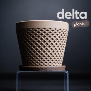 May include: A tan-colored planter with a diamond-patterned exterior and a matching saucer. The planter has the word "delta" in white text and the word "planter" in a brown rectangle.