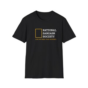 Może przedstawiać: Czarny t-shirt z napisem "NATIONAL SARCSM SOCIETY" w kolorze białym, z żółtym kwadratem i frazą "LIKE WE NEED YOUR SUPPORT." Koszulka ma okrągły dekolt i krótkie rękawy.