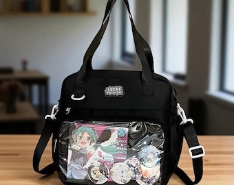 May include: Black tote bag with a clear front pocket displaying anime-style artwork and pins. The bag has a top handle, a detachable shoulder strap, and the text "LUCKY FASHION" on a patch.
