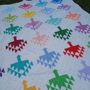 May include: A white quilt featuring a repeating pattern of multi-colored bird-shaped motifs. The birds are arranged in a grid and appear in various colors including red, yellow, green, blue, orange, purple, and pink, all stitched onto a white fabric.