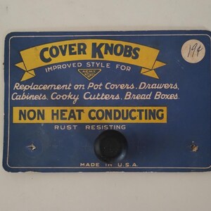 May include: A vintage blue and yellow sign for "COVER KNOBS" with text indicating they are for pot covers, drawers, and cabinets. The sign also states they are non-heat conducting and rust-resistant. A black knob is attached.