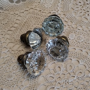 May include: Four vintage glass doorknobs with faceted crystal-like designs. The knobs have a clear, reflective appearance and are mounted on aged brass hardware. The arrangement suggests a focus on antique home decor or restoration projects.
