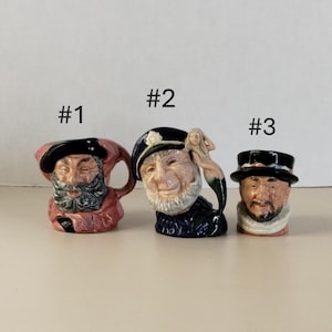 May include: Three ceramic figurines depicting bearded men with hats. The figurines are numbered #1, #2, and #3. The first is a pitcher with a red and black design. The second is a sailor with a mermaid. The third is a small figurine with a black hat.