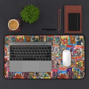 May include: A rectangular desk mat featuring a collage of vintage Japanese comic book covers with monster illustrations. A laptop, white mouse, and other office supplies are on the mat. A cup of coffee and a small plant are also visible.