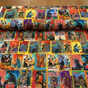 May include: A bolt of cotton fabric featuring a repeating grid pattern of vintage Godzilla movie posters. Each rectangular panel displays colourful illustrations of the monster in various action scenes, with Japanese text and movie titles.