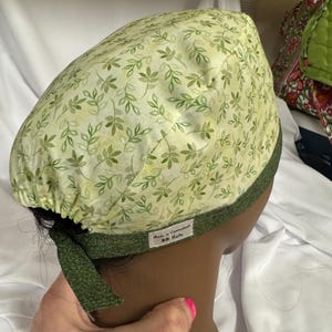 Op de afbeelding: Een lichtgroene operatiemuts met een patroon van groene bladeren. De muts heeft een donkergroene rand en strikbanden. Het label luidt "Made in Connecticut BB Hats".