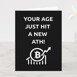 Könnte beinhalten: Schwarze Grußkarte mit weißem Text: "YOUR AGE JUST HIT A NEW ATH!". Unter dem Text befindet sich ein Bitcoin-Symbol mit einem Pfeil nach oben. Im Hintergrund eine weiße Gänseblümchen in einer Glasvase.