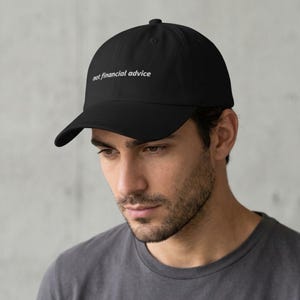 Könnte beinhalten: Eine schwarze Baseballkappe mit dem weiß gestickten Text not financial advice auf der Vorderseite. Die Kappe hat einen gebogenen Schirm, eine strukturierte Krone mit einem Knopf oben und ein klassisches Sechs-Panel-Design mit Ösen.