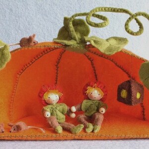 May include: A felt pumpkin playhouse with a green vine and leaves. Two small felt dolls with red hair and green clothing are sitting inside the pumpkin. Two small felt mice are outside the pumpkin.