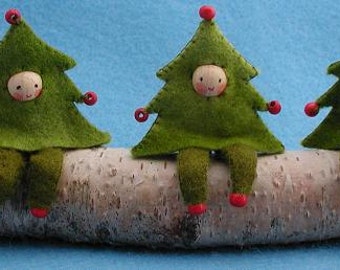 May include: Three felt Christmas tree ornaments with red accents sit on a birch log. Each tree has a wooden face with a painted smile.