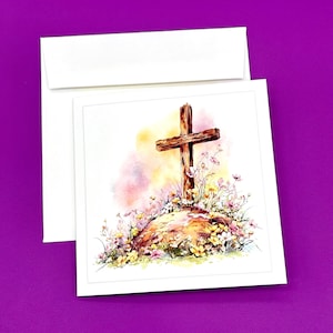 May include: A watercolor greeting card featuring a wooden cross on a small hill with colorful wildflowers. The card is inside a white envelope, set against a purple background. The artwork has soft, blended colors.